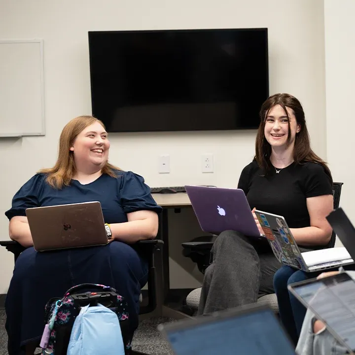 Two students with laptops talking and laughing.