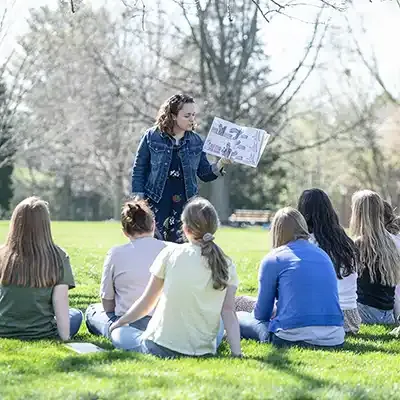 Professor teaching class outdoors in a grassy shaded setting.