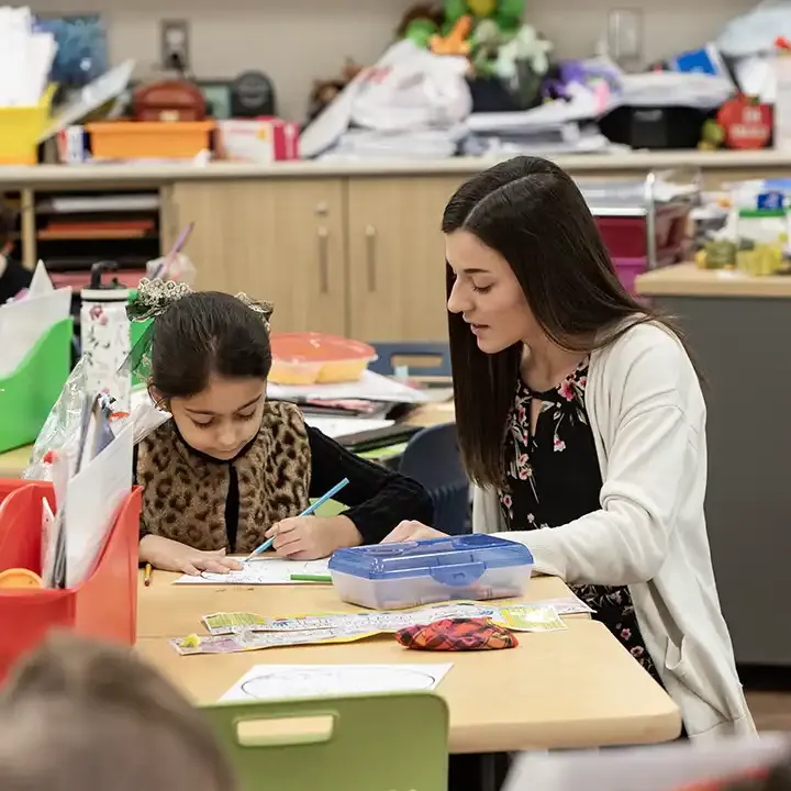 Female teacher educating a young student at a table drawing with colored pencils