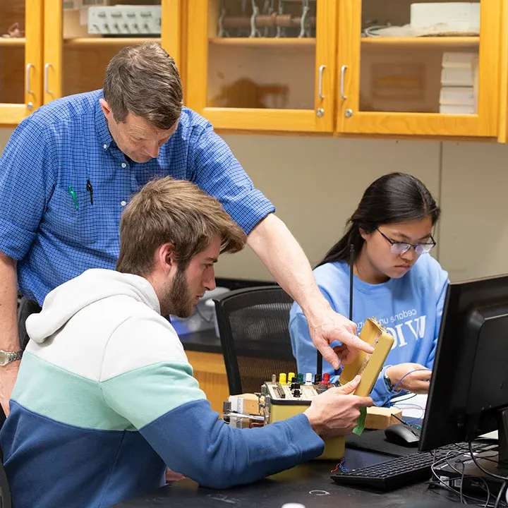 Professor working with students in an electronics lab.