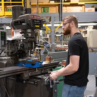 Male student doing metal work using a large milling machine.