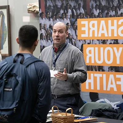 Missions conference, missionary table host speaking with student.